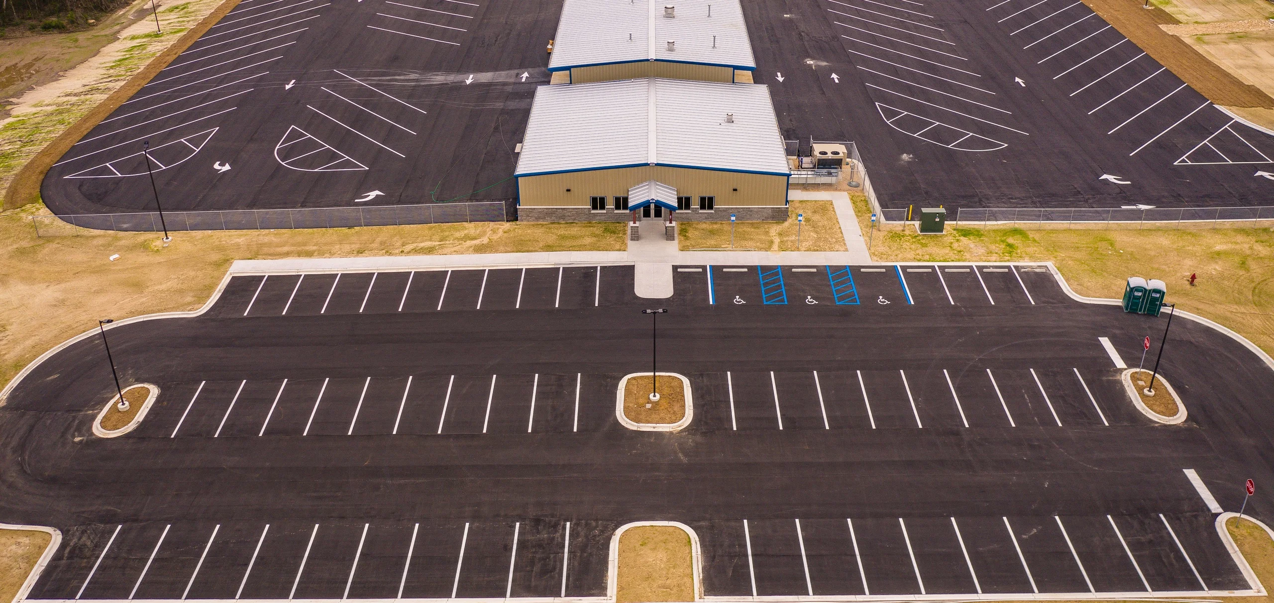 Wide aerial view of a complete newly paved commercial parking lot with freshly painted stalls, directional arrows and ADA accessible spaces, striped by American Curb Appeal in Tallahassee, FL